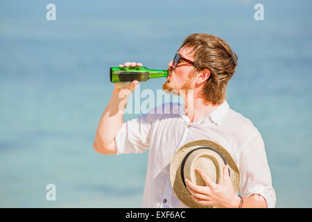 Mann mit Hut und Sonnenbrille Enjoing Bier in der Flasche am Strand Stockfoto