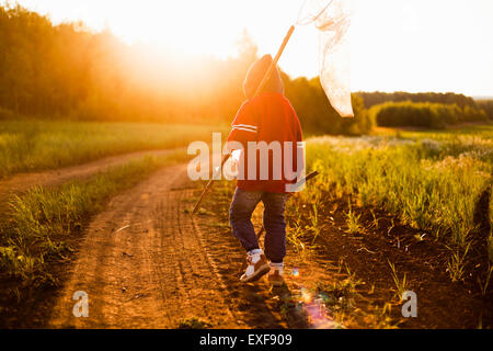 Rückansicht des jungen mit dem Schmetterling net gehen auf Feldweg bei Sonnenuntergang, Sarsy Dorf, Swerdlowsk, Russland Stockfoto