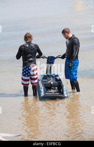 Zwei junge Männer in Bermuda-Shorts im Meer festhalten an Jet-Ski Swanage im Juni stehen Stockfoto