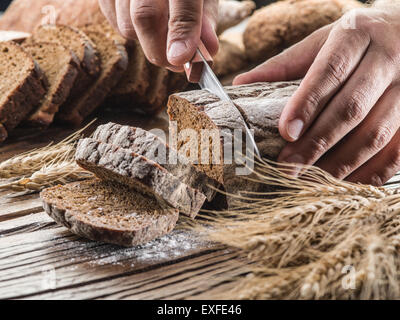 Die Hände des Mannes Schneiden von Brot auf das Holzbrett. Stockfoto