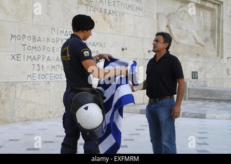 Athen, Griechenland. 13. Juli 2015. Ein Aufruhr Polizist kehrt die griechische Flagge in der Demonstrant. Griechen versammelten sich vor dem griechischen Parlament unter dem Banner der "verlassen wir dieses Europa". Sie forderten die Regierung auf die Forderungen der griechischen Gläubiger für weitere Sparmaßnahmen nicht nachgeben, sondern um die Eurozone zu verlassen. Bildnachweis: Michael Debets/Alamy Live-Nachrichten Stockfoto