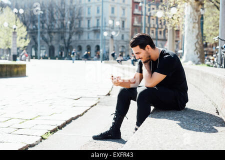 Schöne italienische Junge sitzt auf einem Bürgersteig mit dem Smartphone verbunden online - Sozialnetz, Technologie-Konzept Stockfoto