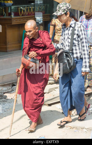 Yangon, Myanmar-Mai 5. 2014: ein Mann hilft einen blinden Mönch auf der anderen Straßenseite. Mönche sind ein alltäglicher Anblick in der Stadt. Stockfoto