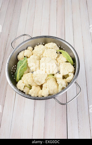 Vertikale erhöhte Ansicht eines Kopfes von Blumenkohl in einem Metall Sieb auf einem rustikalen Holztisch mit Textfreiraum. Stockfoto