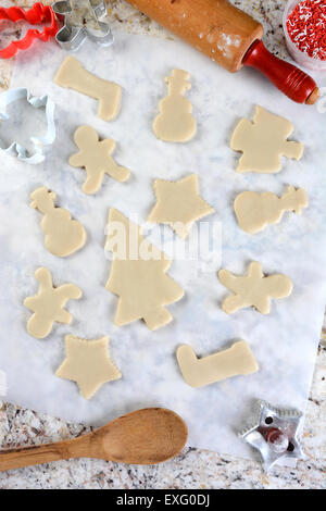 Weihnachtsplätzchen Formen auf Pergamentpapier. Im Umkreis sind Messer, Wanne mit Streuseln, Löffel und Nudelholz. Vertikal Stockfoto