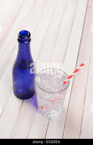 Hohen Winkel Schuss ein Glas voller Wasser und Eis und rot und weiß Stroh neben einer blauen Flasche zu trinken. Hochformat mit co Stockfoto