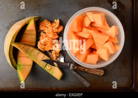 Hohen Winkel Schuss aus einer Schüssel voller Melone Stück neben dem Rinden und Samen. Messer und Löffel sind auch auf dem Metall Küchen Stockfoto