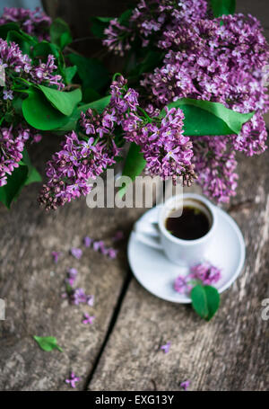 Lila Blumen in einer Vase und eine Tasse Kaffee auf dem rustikalen Stil-Hintergrund Stockfoto