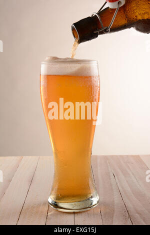 Bier in ein hohes Glas von einer Swing-Top-Flasche gießen. Auf einem Holztisch mit einem dunklen Hintergrund ot. Stockfoto