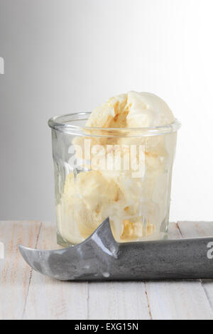 Glas von Vanilla Ice Cream und Schaufel auf einem Holztisch mit einer leichten bis dunkelgrauen Hintergrund. Stockfoto