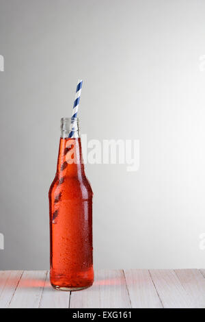 Eine einzige Flasche Erdbeer Soda auf einem Holztisch gegen eine leichte bis dunkelgrauen Hintergrund. Die Flasche hat einen blauen und weißen drin Stockfoto