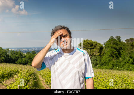 Hübscher Mann mittleren Alters mit Salz Pfeffer Haar gekleidet mit Sport-Shirt hält seinen Kopf in den Feldern der italienischen Landschaft: er scheint Kopfschmerzen haben Stockfoto