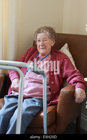 Bildnis einer älteren Dame sitzt in einem Sessel in ein Pflegeheim mit ihren remote-Unterstützung um den Hals. Stockfoto