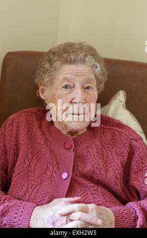 Bildnis einer älteren Dame sitzt in einem Sessel in eine Pflege, die auf der Suche nach Hause direkt auf Kamera Stockfoto