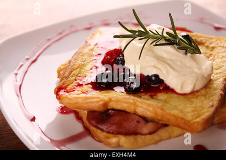 Leckere French-Toast mit Speck Sirup Beeren und Sahne auf einem weißen Teller auf einem Holztisch. Stockfoto