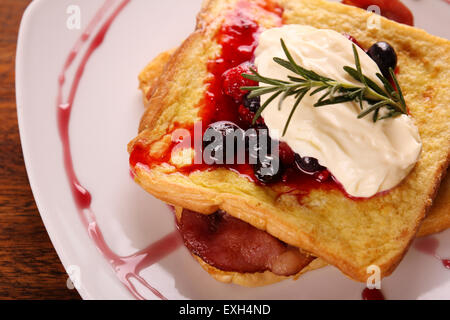 Leckere French-Toast mit Speck Sirup Beeren und Sahne auf einem weißen Teller auf einem Holztisch. Stockfoto