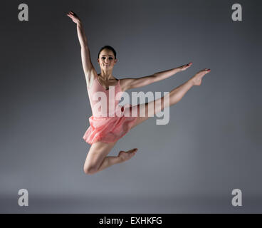 Schöne weibliche Ballett-Tänzerin auf einem grauen Hintergrund. Ballerina ist barfuß und trägt eine orange Kleid und Anzug. Stockfoto