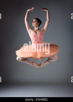 Schöne weibliche Ballett-Tänzerin auf einem grauen Hintergrund. Ballerina trägt eine orange Tutu, rosa Strümpfe und Spitzenschuhe. Stockfoto