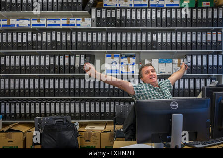 Mann, die Dehnung beim Sitzen am Schreibtisch bei der Arbeit, Reykjavik, Island Stockfoto