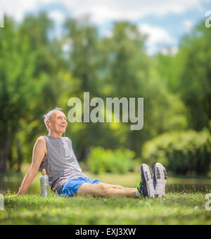 Aktive senior woman Sportswear auf dem Rasen im Park sitzen und hören von Musik über Kopfhörer mit Tilt-Shift-Objektiv geschossen Stockfoto