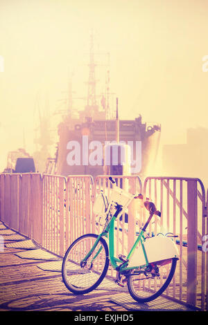 Vintage getönten Fahrrad geparkt Pier mit Schiff in der Ferne, Sonnenuntergang Lens-Flare-Effekt. Stockfoto