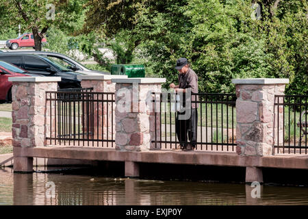 Ein kaukasier, der in seinen 60ern auf einem Pier steht, wirft in einem Teich im will Rogers Park in Oklahoma City, Oklahoma, USA, Karpfenfische mit Nahrung. Stockfoto