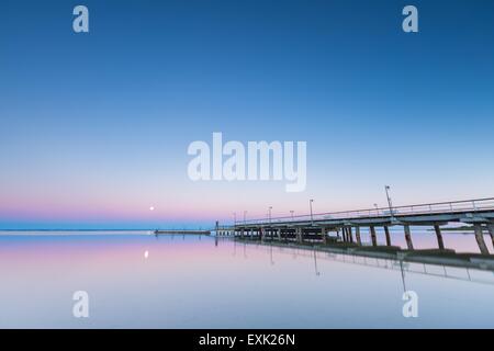 Landschaft für Gdanska Bucht mit Mole in Jastarnia vor Sonnenaufgang fotografiert. Landschaft mit Pastell-Farben des Sonnenaufgangs. Mond, settin Stockfoto