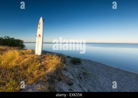 Weißen Surf Board schlug im Sand am Ufer des Meeres mit goldenen Sonnenaufgang Licht. Schöne Landschaft der polnischen Küste Stockfoto