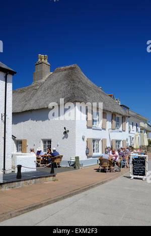 Torcross, Devon, UK.  Leute sitzen in der Sonne in einem ziemlich strohgedeckten Café bei Torcross in Devon. Stockfoto