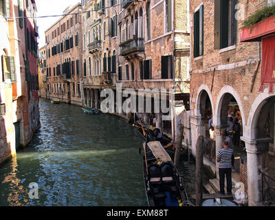 Gondel vertäut in einem schmalen Kanal mit dem Gondoliere warten auf Touristen in Venedig mit schönen Häusern an den Seiten. Venedig. Italien. Stockfoto