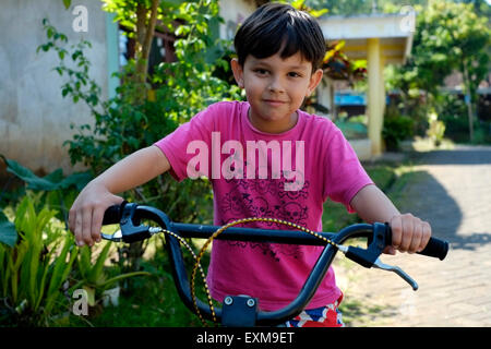 sieben Jahre alten kleinen Jungen auf seinem Fahrrad in einer Dorfstraße in Java Indonesien spielen Stockfoto