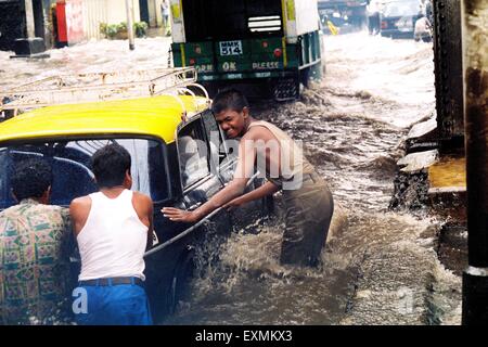 Menschen schieben ein Taxi gestrandet in den überfluteten Gewässern durch heftige Regenfälle am König Circle in Bombay jetzt Mumbai; Maharashtra; Indien Stockfoto