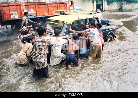 Straßenkinder drängen auf das schiebende Taxi, das aufgrund des Monsunregens am King Circle in Bombay Mumbai Maharashtra India Asia in der überfluteten Straße gestrandet ist Stockfoto