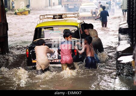 Straßenkinder drücken ein Taxi gestrandet in den überfluteten Gewässern durch heftige Regenfälle am König Circle in Bombay jetzt Mumbai Stockfoto