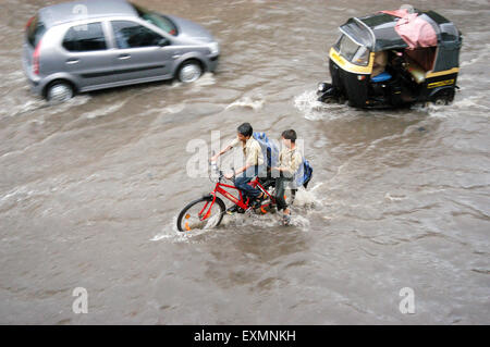 Schule Jungs fahren Fahrrad Auto Rikscha Monsun Regen Autofahren Wasser überflutete Straße Vidyavihar Mumbai Indien Stockfoto