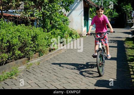 sieben Jahre alten kleinen Jungen auf seinem Fahrrad in einer Dorfstraße in Java Indonesien spielen Stockfoto