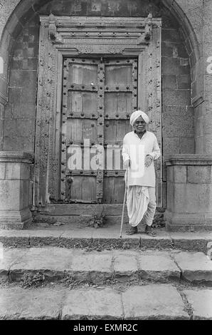 Alter Mann steht vor massiven Vorfahren Hause mit kunstvoll geschnitzten Tür in Munagoli Dorf Bijapur Karnataka Indien Stockfoto