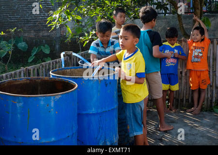 junge Dorfkinder spielen mit Wasser aus großen Öl-Trommeln in einem ländlichen Dorf in Java Indonesien Stockfoto