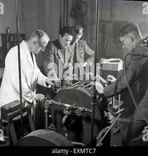 1950er-Jahren, historische, beschichteten jungen Erwachsenen männlichen Studenten der Ingenieurwissenschaften oder Lehrlinge wird gezeigt, wie man eine Maschine zu bedienen durch eine weiße, Lehrer oder Betreuer. Stockfoto