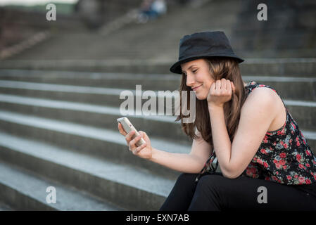 Deutschland, Koblenz, Deutsches Eck, junge Frau mit Handy sitzt auf der Treppe Stockfoto