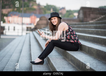 Deutschland, Koblenz, Deutsches Eck, junge Frau mit Handy sitzt auf der Treppe Stockfoto