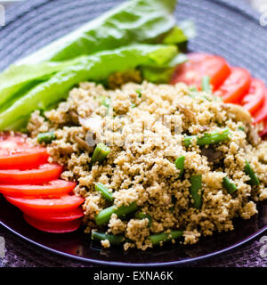 Ein Teller mit Couscous mit Basilikum und Gewürzen serviert mit Tomatenscheiben und Salat Blätter auf einem lila transparent Teller Stockfoto