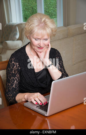 Ältere Frau in einem schwarzen Kleid sitzt an einem Tisch mit einem Laptop Computer alte Dame mit Hilfe moderner Technologie Stockfoto