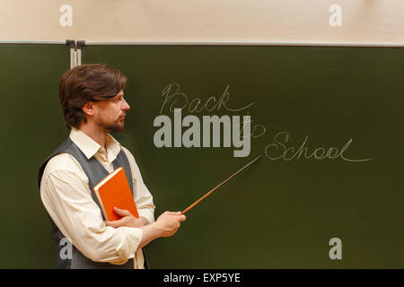 Der Lehrer zeigt die Inschrift auf der Rückseite zur Schule. Die Inschrift auf der Tafel mit Kreide. Stockfoto