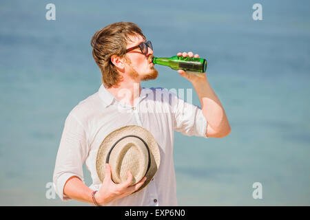 Mann mit Hut und Sonnenbrille Enjoing Bier in der Flasche am Strand Stockfoto