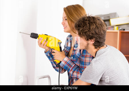Paar renovieren zusammen als Frau mit Mann stand neben ihr beobachten Bohrmaschine an Wand Stockfoto