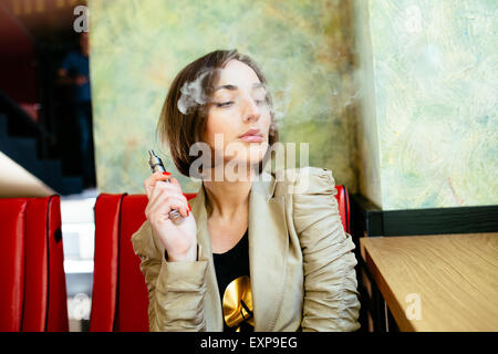 Mädchen sitzt und raucht elektronische Zigarette Stockfoto