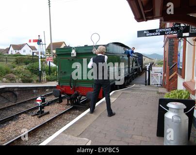 West Somerset Railway. Dampfzug nähert sich Blue Anchor Station, Somerset, Großbritannien. Der Stationswächter hält den Sicherheitsschlüssel hoch, um den Sicherheitsschlüssel beim Vorbeigehen abzuholen Stockfoto