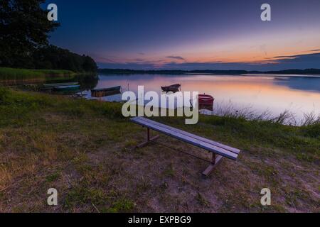 Schöner See Sonnenuntergang mit Fischer Boote und Bank am Ufer. Polnischen See in Masuren. Polnische Seenlandschaft Stockfoto