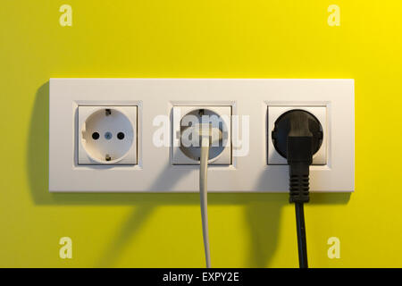 Eine europäische Mehrfachsteckdose (drei Steckdosen) In Österreich mit einem grauen und schwarzen Stecker eingesteckt Und Kabel und eine gelbe Wand dahinter Stockfoto